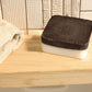 Lavender exfoliating soap bar with upcycled coffee grounds and natural oils on wooden surface next to beige towel